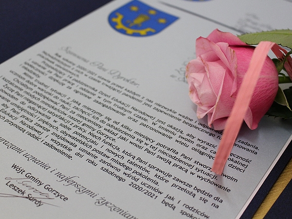 Zdjęcie treści podziękowania, jakie otrzymali dyrektorzy i nauczyciele podpisane przez Wójta Gminy Gorzyce - Leszka Surdego. Na kartce podziękowań leży róża w kolorze różowym, przewiązana wstążeczka w tym samym kolorze.