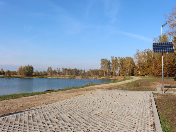 Zbiornik wodny w Trześni, na pierwszym planie widać parking, dalej okalającą zbiornik drogę oraz latarnię słoneczną