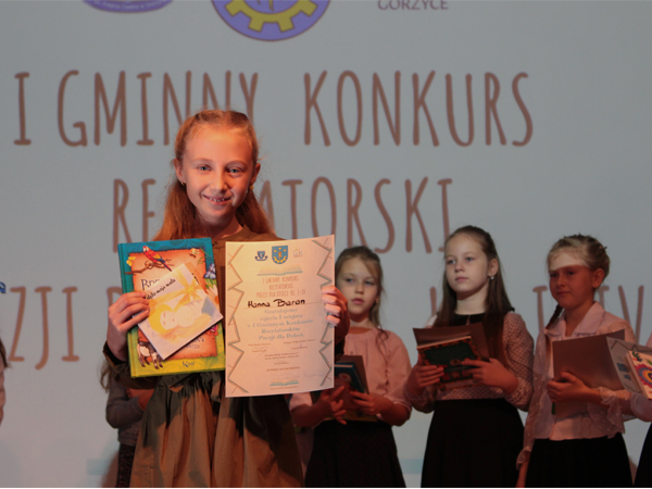 Zwycięzczyni w II kategorii wiekowej - Hanna Baran. W rękach trzyma książkę i dyplom, w tle stoją uczestnicy konkursu