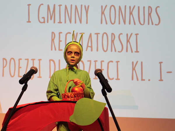 Na zdjęciu dziewczynka w zielonym kostiumie interprerująca wiersz "Entliczek Pentliczek"